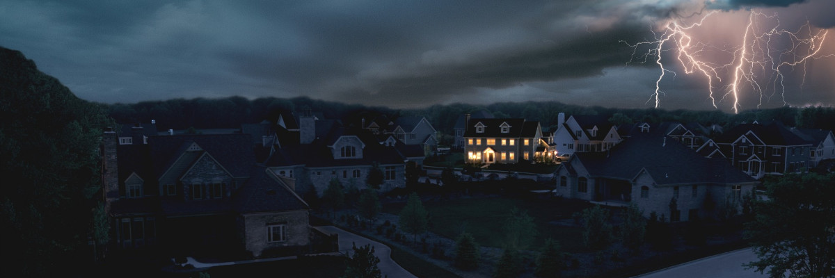 Lightning flashes from cloud to ground over a dark neighborhood where only a single home has lights powered by a standby generator.