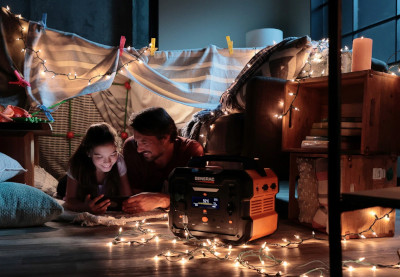 A couple surrounded by fairy lights lay on the wooden floor of their bedroom and look at a tablet during a power outage.