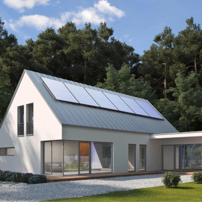 12 solar panels mounted on the roof of a modern home. The blue sky has a few small puffy clouds and the home is surrounded by trees.