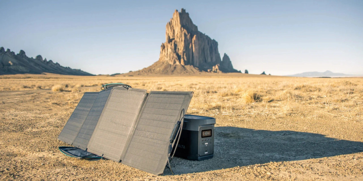A power station sits in the shade of a foldable solar panel while charging in the desert sun.